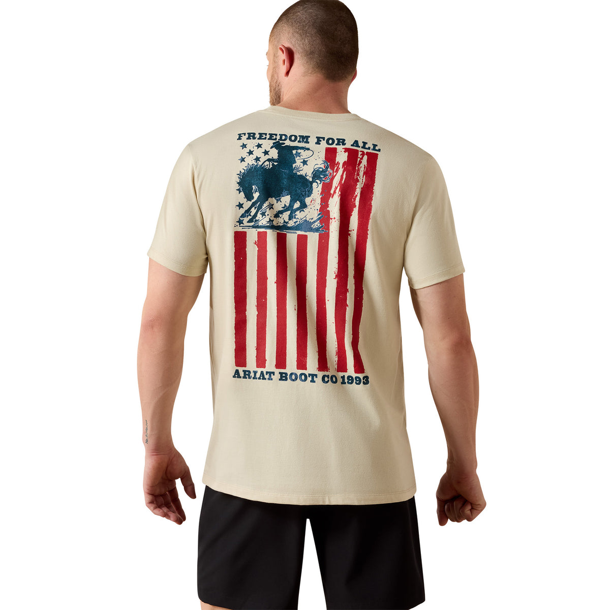 Man wearing a beige t-shirt with an American flag and horse graphic, brand 'Ariat' visible.