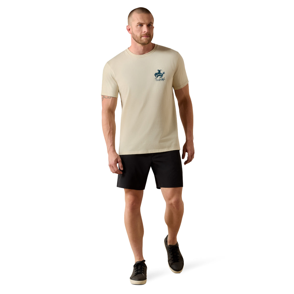 Man wearing a beige t-shirt with a logo and black shorts on a white background