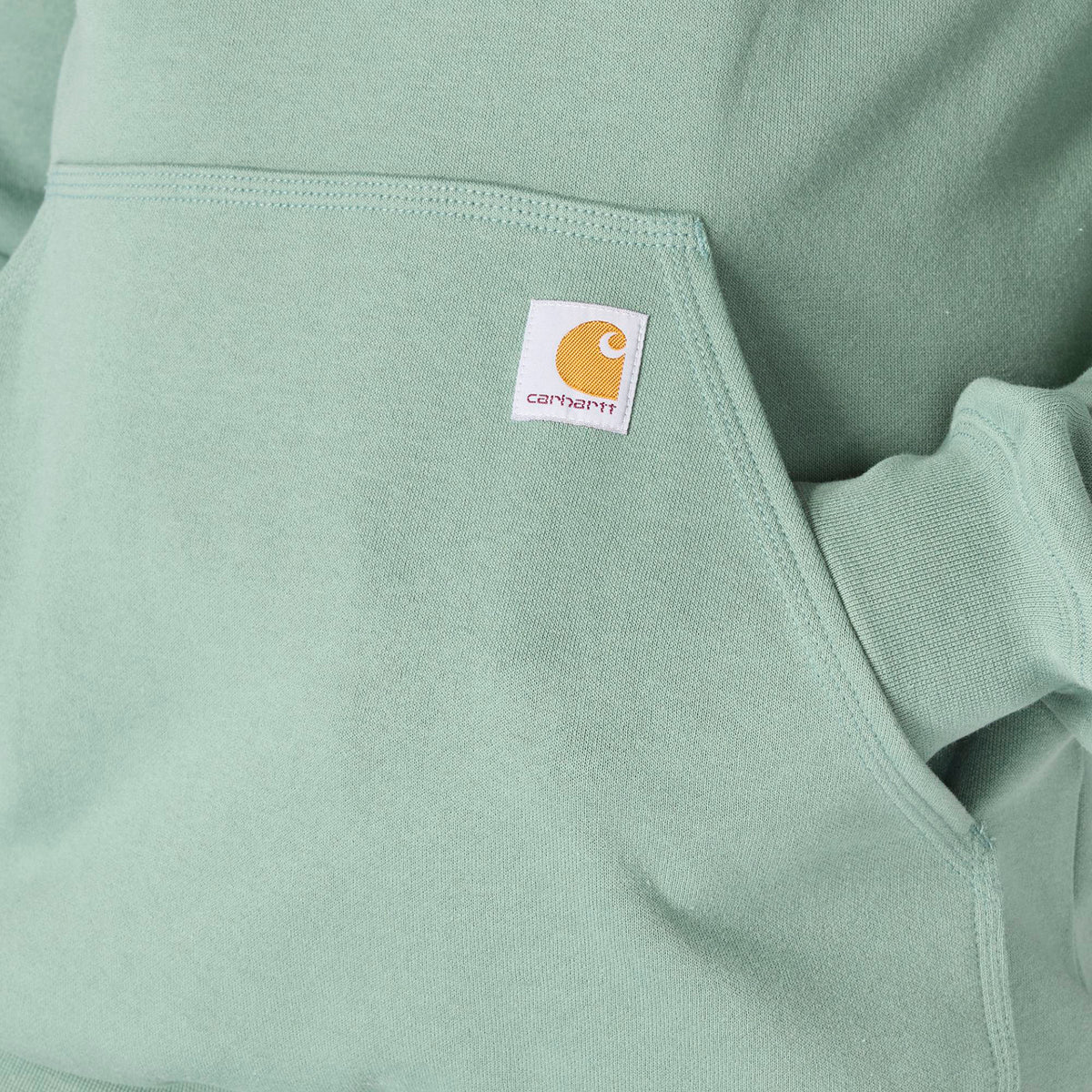 Close-up of a light green hoodie with a Carhartt logo on the chest pocket.